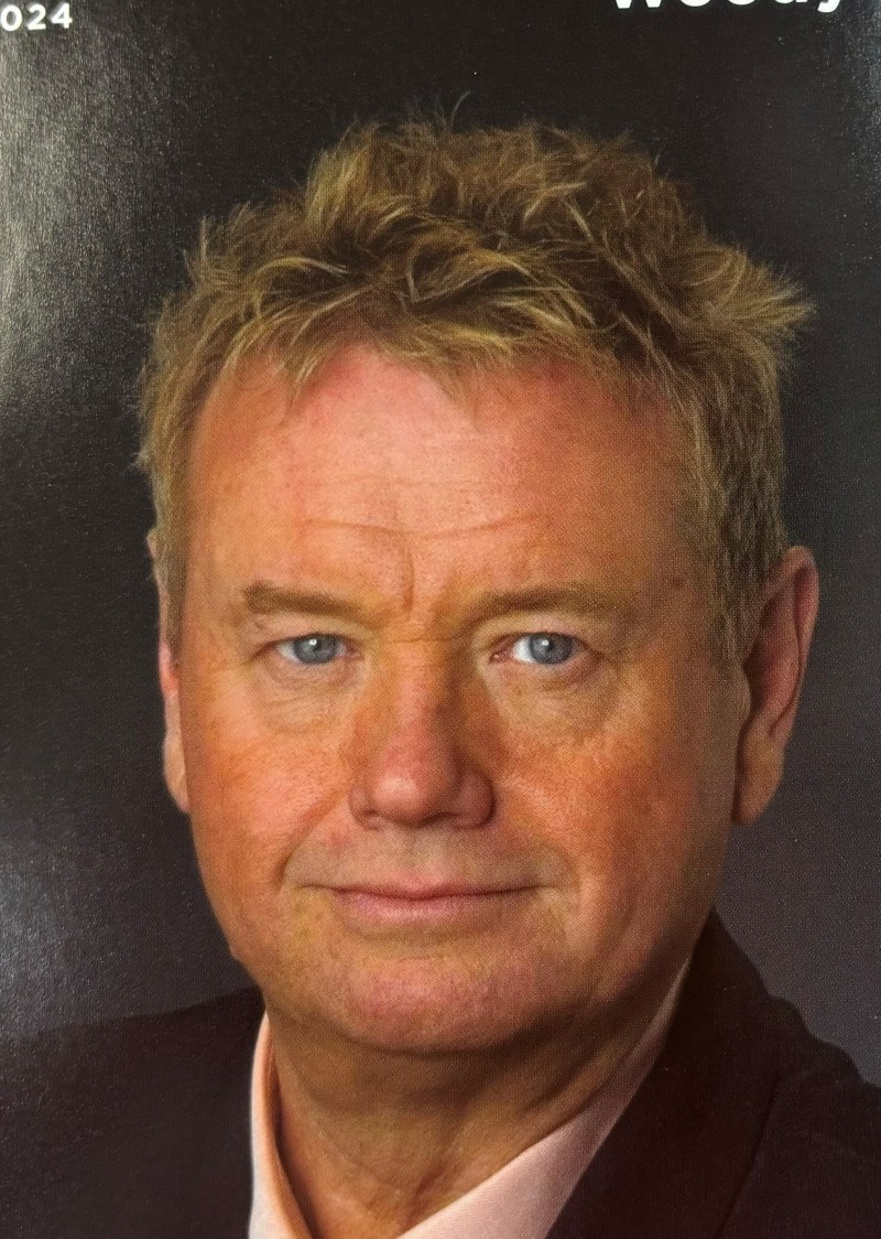 Woody Paige wearing a suit and tie smiling at the camera