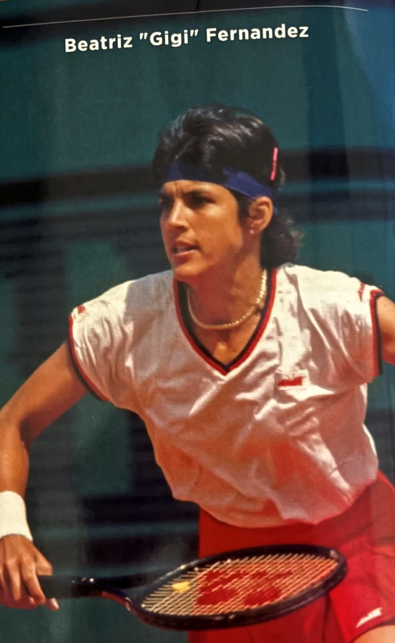 Tennis player in action wearing a white shirt and red shorts, holding a racket.