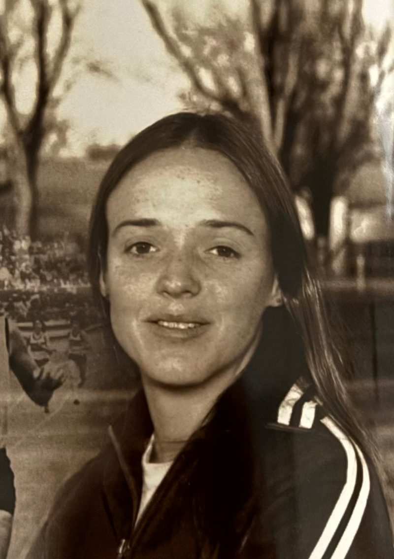 Sepia photo of a young person with long hair wearing a jacket, trees in the background.