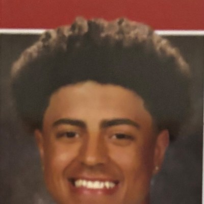 Smiling person with afro hairstyle, wearing earrings.